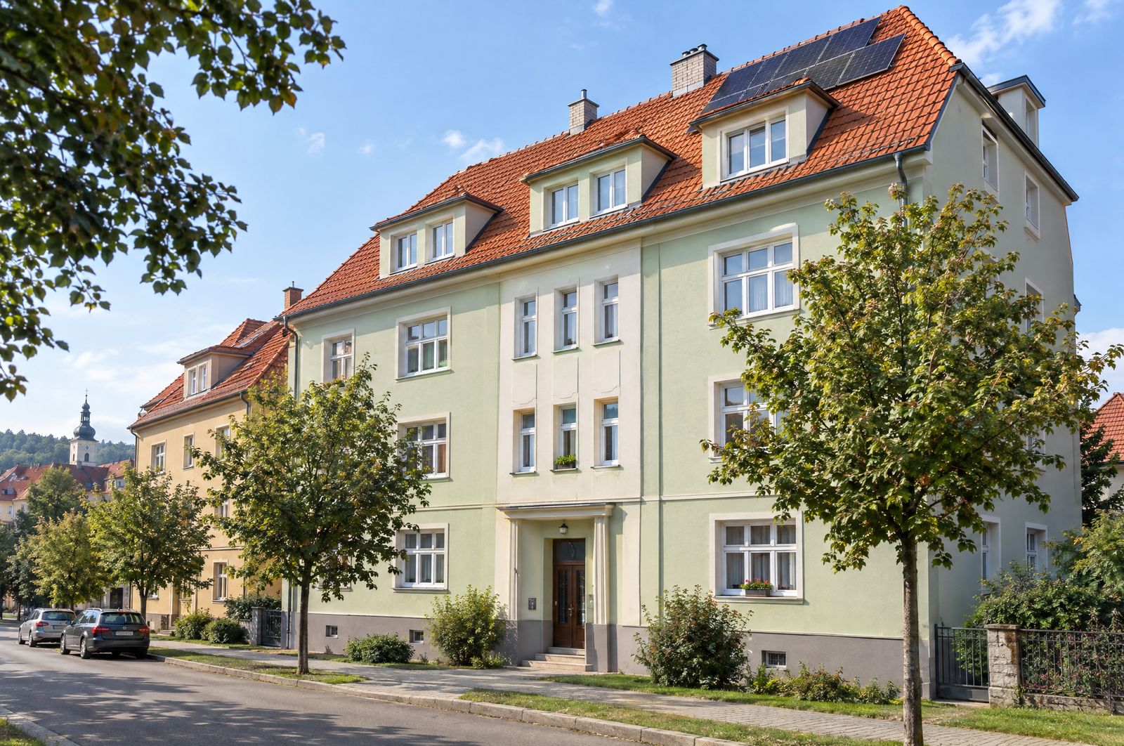 Opravený bytový dům s červenou střechou a solárními panely